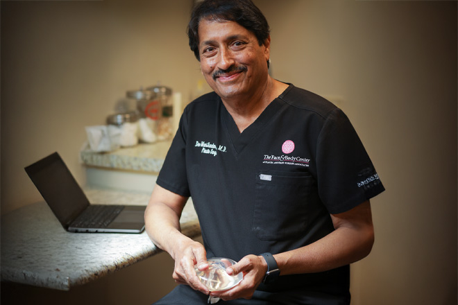 Dr. Dev ManiSundaram in scrubs holding breast implants in Flowood practice